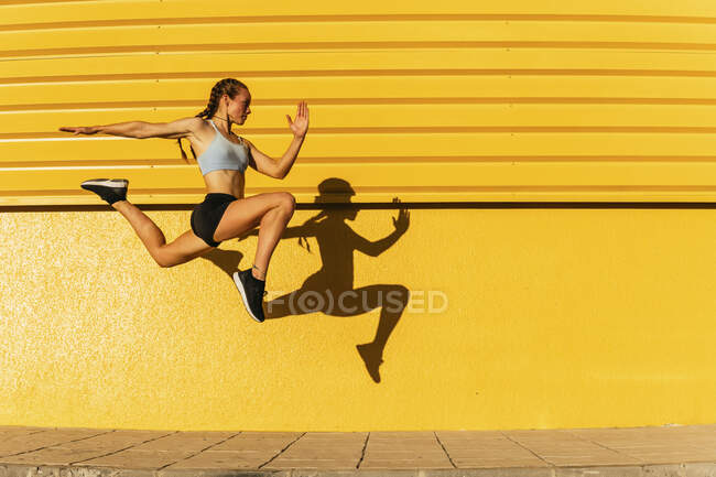 Atleta feminina se exercitando enquanto saltava pela parede amarela durante o dia ensolarado — Fotografia de Stock