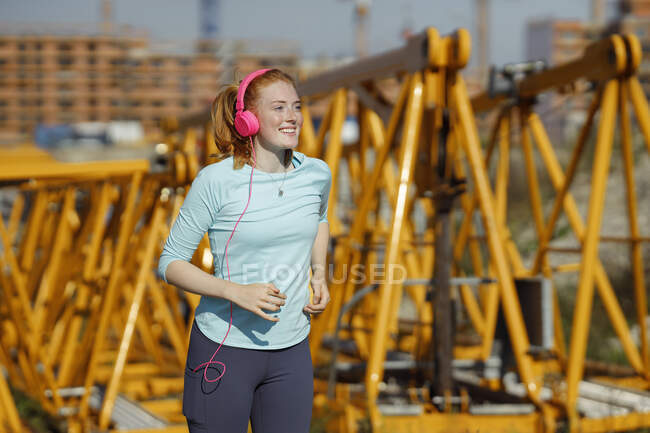 Junge Frau mit Kopfhörern läuft auf Baustelle — Stockfoto