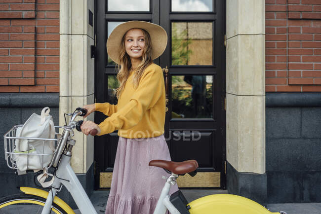 Schöne Frau schaut weg, während sie mit Fahrrad vor der Tür steht — Stockfoto