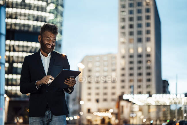 Hombre de negocios sonriente trabajando en la tableta digital en la ciudad - foto de stock