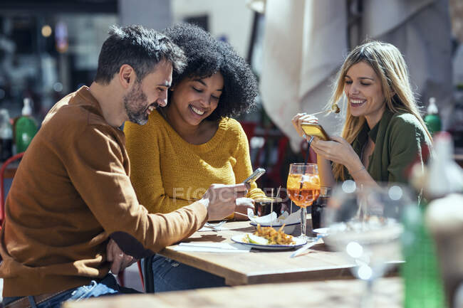Amis masculins et féminins utilisant des téléphones mobiles au restaurant — Photo de stock
