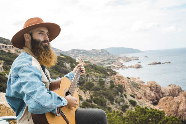 Чоловік у капелюсі грає на гітарі, дивлячись на — стокове фото