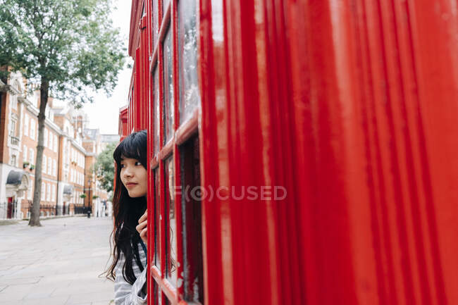 Woman hiding behind telephone booth in city — Stock Photo