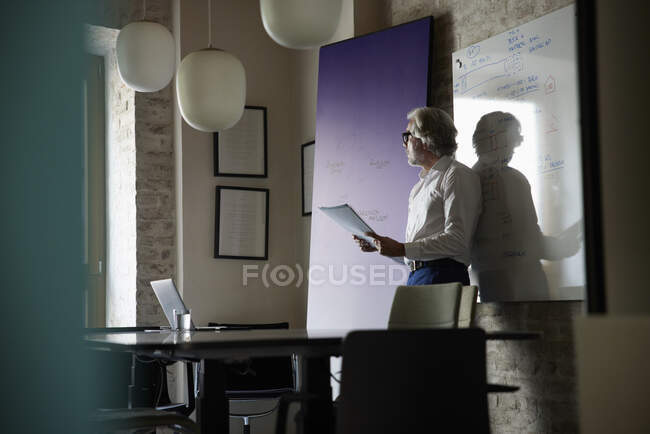 Empresario con documentos de pie frente a pizarra en la oficina - foto de stock