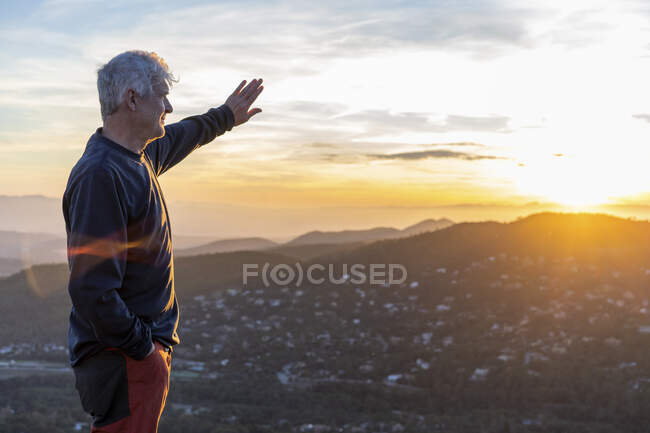 Старший мужчина защищает глаза, стоя на горе во время заката — стоковое фото