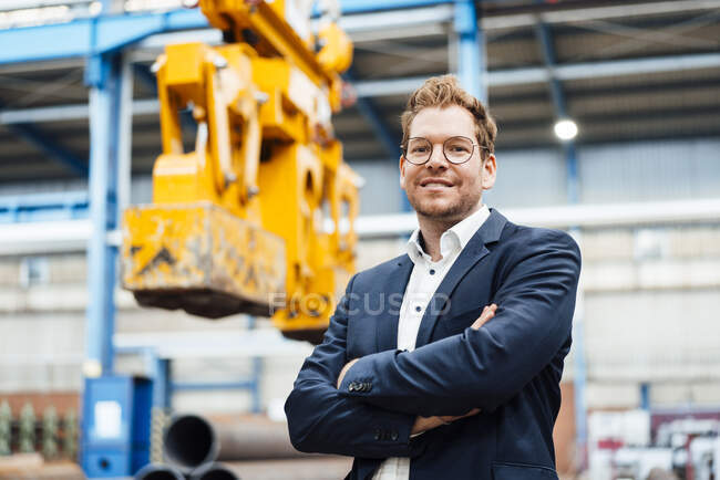 Улыбающийся бизнесмен со скрещенными руками стоит на заводе — стоковое фото
