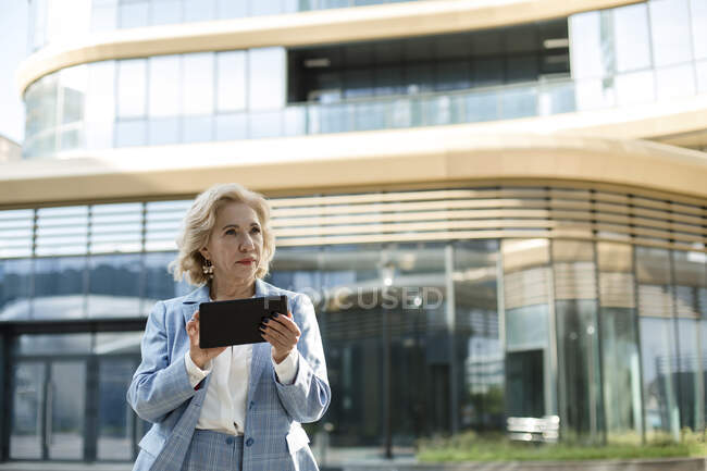 Думливий бізнесмен тримає цифрову табличку, стоячи біля офісного будинку. — стокове фото