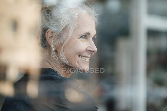 Улыбающаяся женщина с седыми волосами в кафе через стеклянное окно — стоковое фото
