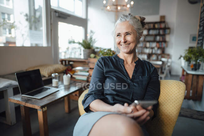 Улыбающаяся деловая женщина с мобильным телефоном сидит в кофейне — стоковое фото