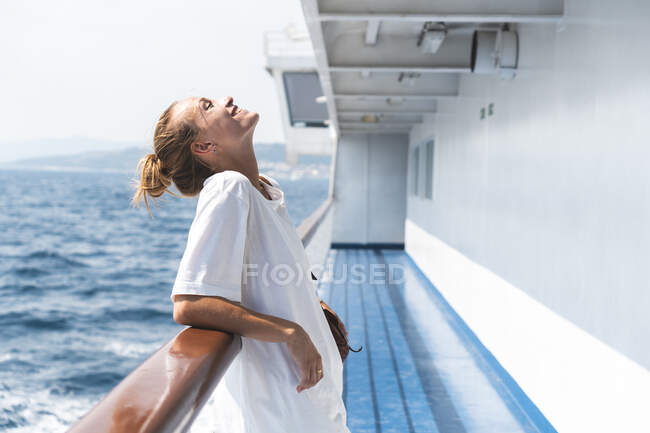 Усміхнена жінка з закритими очима спирається на поручні в човні під час відпустки. — стокове фото
