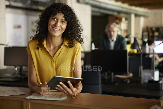 Посмішка бізнесмена з цифровим планшетом спирається на стіл в офісі — стокове фото