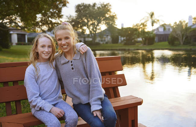 Smiling girls sitting on bench by pond — Stock Photo