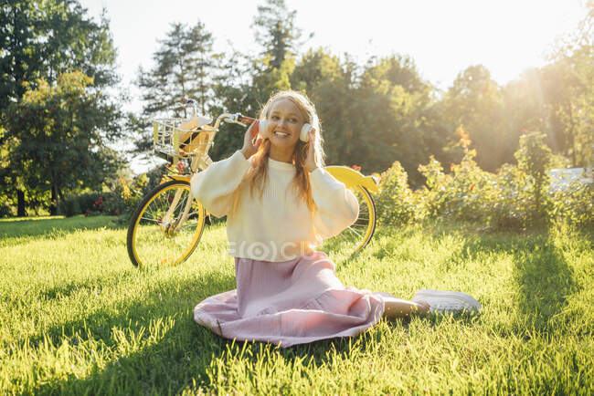 Donna sorridente che ascolta musica sulle cuffie mentre siede sull'erba al parco — Foto stock