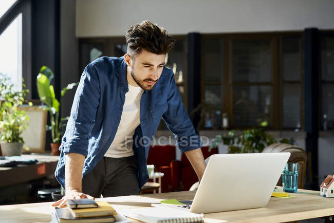 Молодой бизнесмен смотрит на ноутбук в офисе — стоковое фото