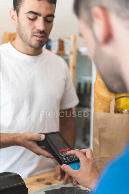 Cliente masculino que ingresa PIN mientras paga con tarjeta de crédito en la tienda - foto de stock