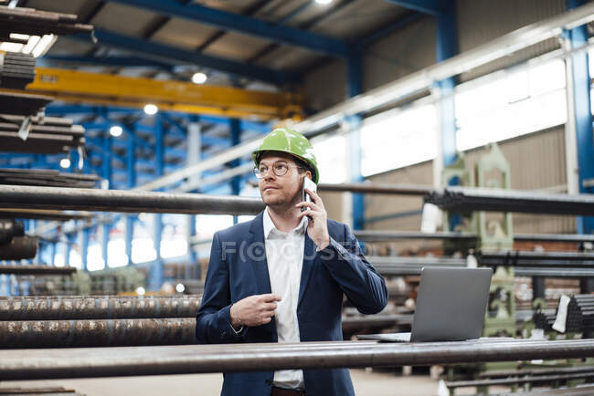 Бізнесмен з хардхатом розмовляє на смартфоні в металургії — стокове фото