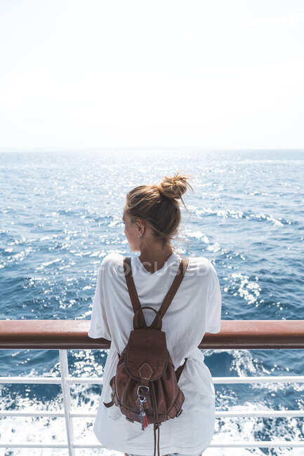 Jovem mulher usando mochila olhando para o mar no barco durante o dia ensolarado — Fotografia de Stock