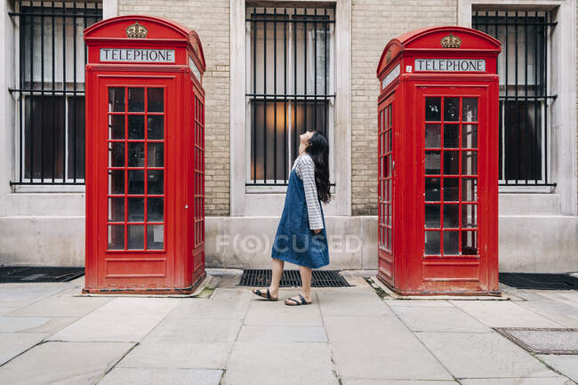 Young woman looking up while standing between telephone booth — Stock Photo