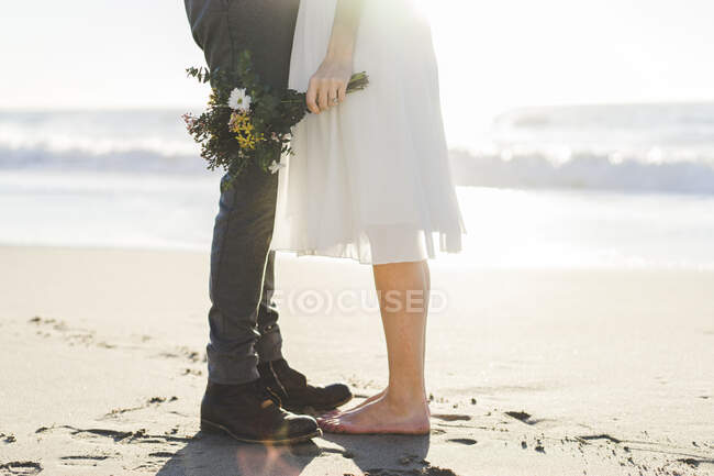 Наречена тримає букет, стоячи з нареченим на пляжі. — стокове фото