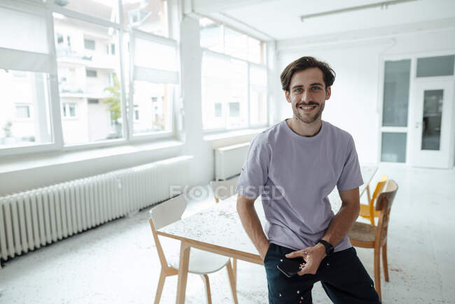 Smiling man with mobile phone sitting on table — Stock Photo