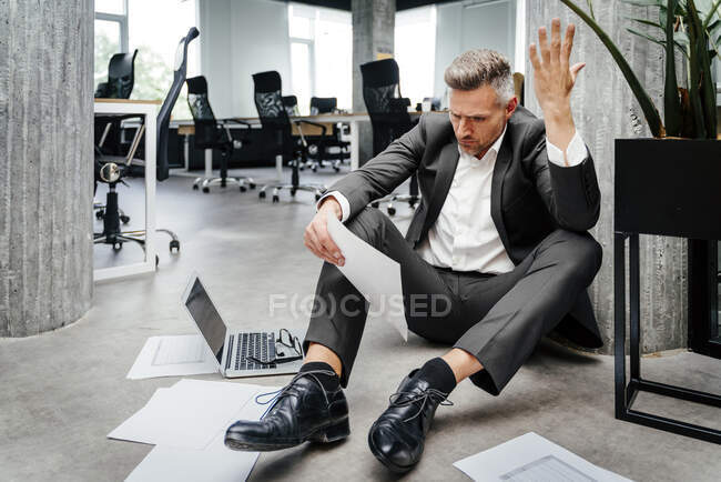 Frustrierter Geschäftsmann gestikuliert beim Blick auf Dokument im Amt — Stockfoto