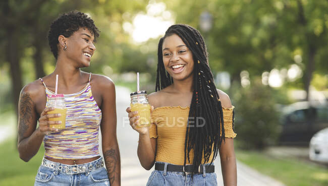 Mujeres alegres disfrutando del jugo en el parque - foto de stock