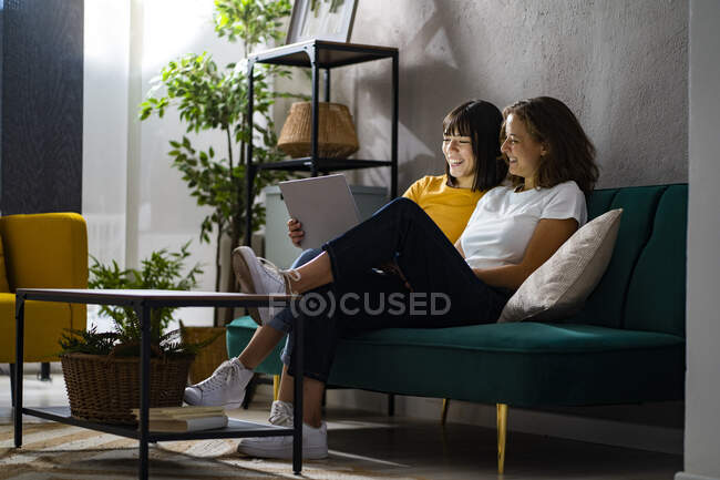 Smiling lesbian couple sharing laptop in living room — Stock Photo