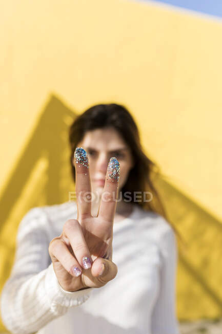 Woman gesturing peace sign with glitter on fingers — Stock Photo
