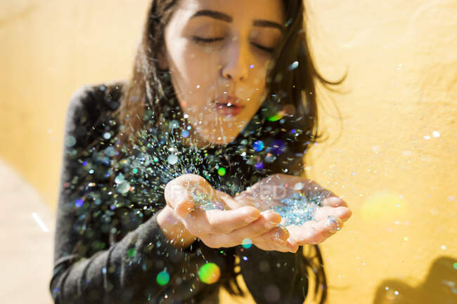 Young woman blowing multi-colored glitter — Stock Photo