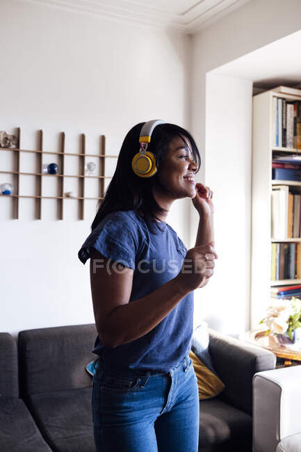 Smiling mid adult woman listening music through wireless headphones while dancing in living room — Stock Photo