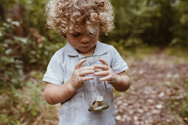 Carino ragazzo in possesso di vaso di vetro con lumache nella foresta — Foto stock
