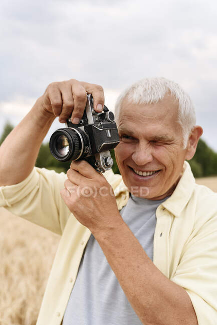 Feliz homem sênior fotografando através da câmera — Fotografia de Stock