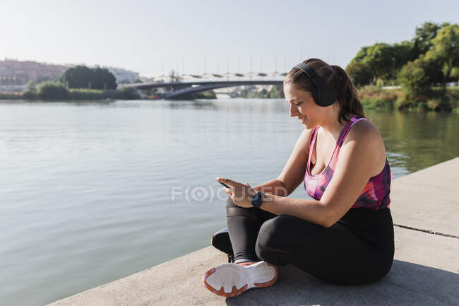 Посмішка спортсменки за допомогою смартфона на березі річки. — стокове фото