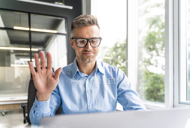 Homme d'affaires professionnel agitant la main pendant l'appel vidéo par ordinateur portable dans le bureau — Photo de stock