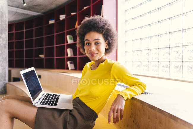 Joven empresaria con portátil apoyada en los escalones de la oficina - foto de stock