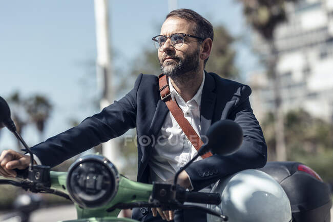 Бизнесмен со шлемом и мешком для перекрестного тела сидит на мотороллере — стоковое фото