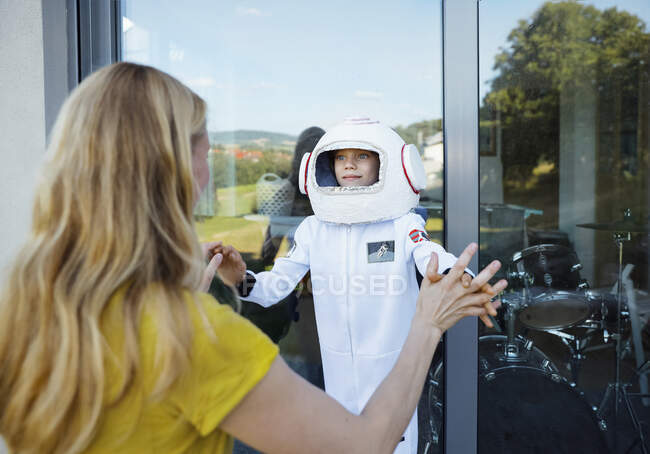 Boy wearing space suit holding hands of mother in front of window — Stock Photo