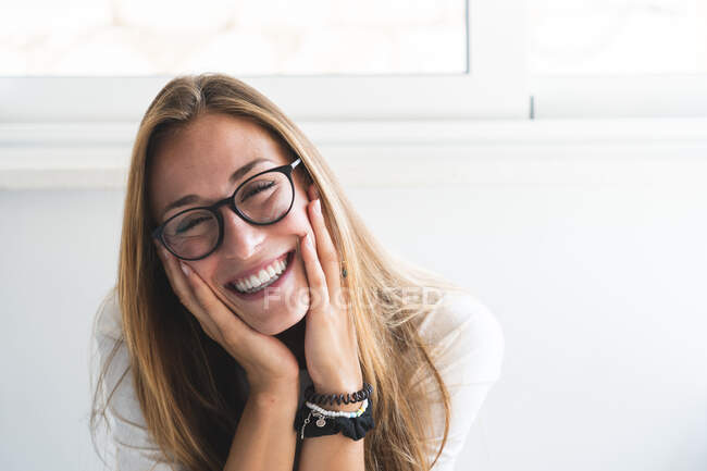 Femme heureuse portant des lunettes assis avec la tête dans la main à la maison — Photo de stock