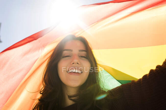 Junge Frau mit Regenbogenfahne bei sonnigem Tag — Stockfoto