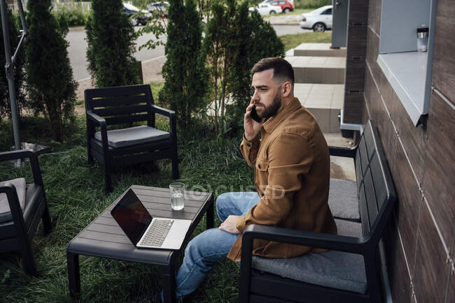 Businessman talking on smart phone while sitting at backyard — Stock Photo