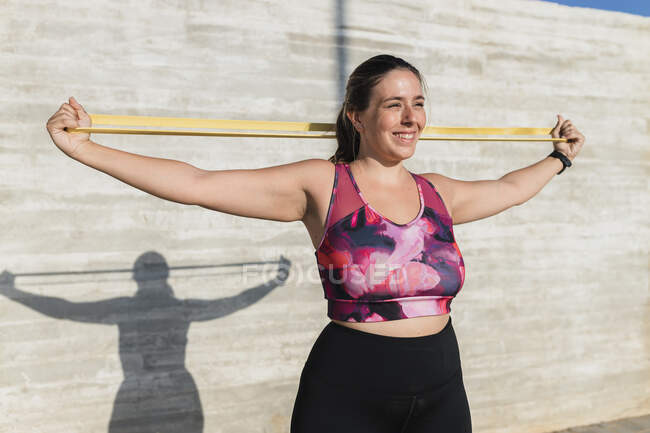 Sportiva sorridente con fascia di resistenza che si allena davanti al muro — Foto stock