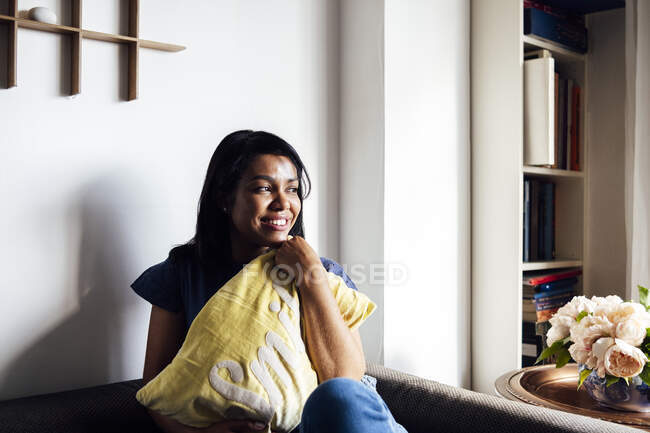 Улыбающаяся женщина сидит с подушкой на диване в гостиной — стоковое фото
