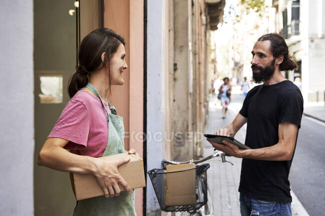 Male delivery person holding digital tablet talking with female entrepreneur outside store — Stock Photo