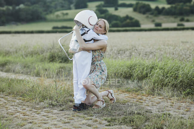Mother hugging son wearing space suit at field — Stock Photo