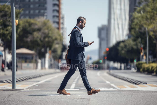 Homme professionnel utilisant un téléphone portable tout en marchant dans la ville — Photo de stock