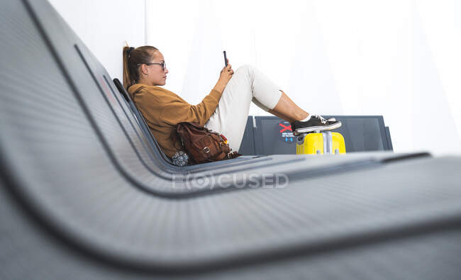 Mulher usando telefone celular enquanto sentado no banco no aeroporto — Fotografia de Stock
