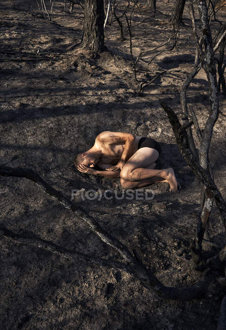 Hombre sin camisa deprimido en posición fetal acostado en el suelo del bosque - foto de stock