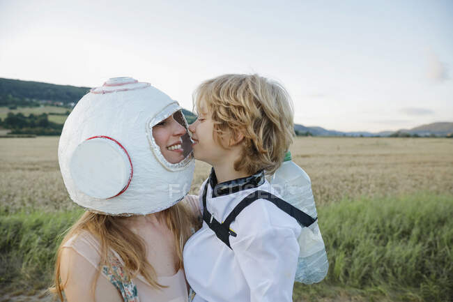 Smiling mother wearing space helmet embracing son at field — Stock Photo