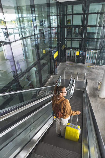 Jovem com bagagem em pé na escada rolante — Fotografia de Stock
