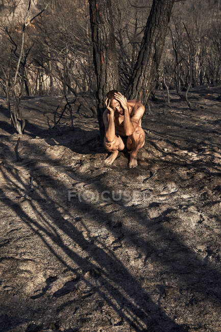 Man crouching with head in hands at burned forest — Stock Photo
